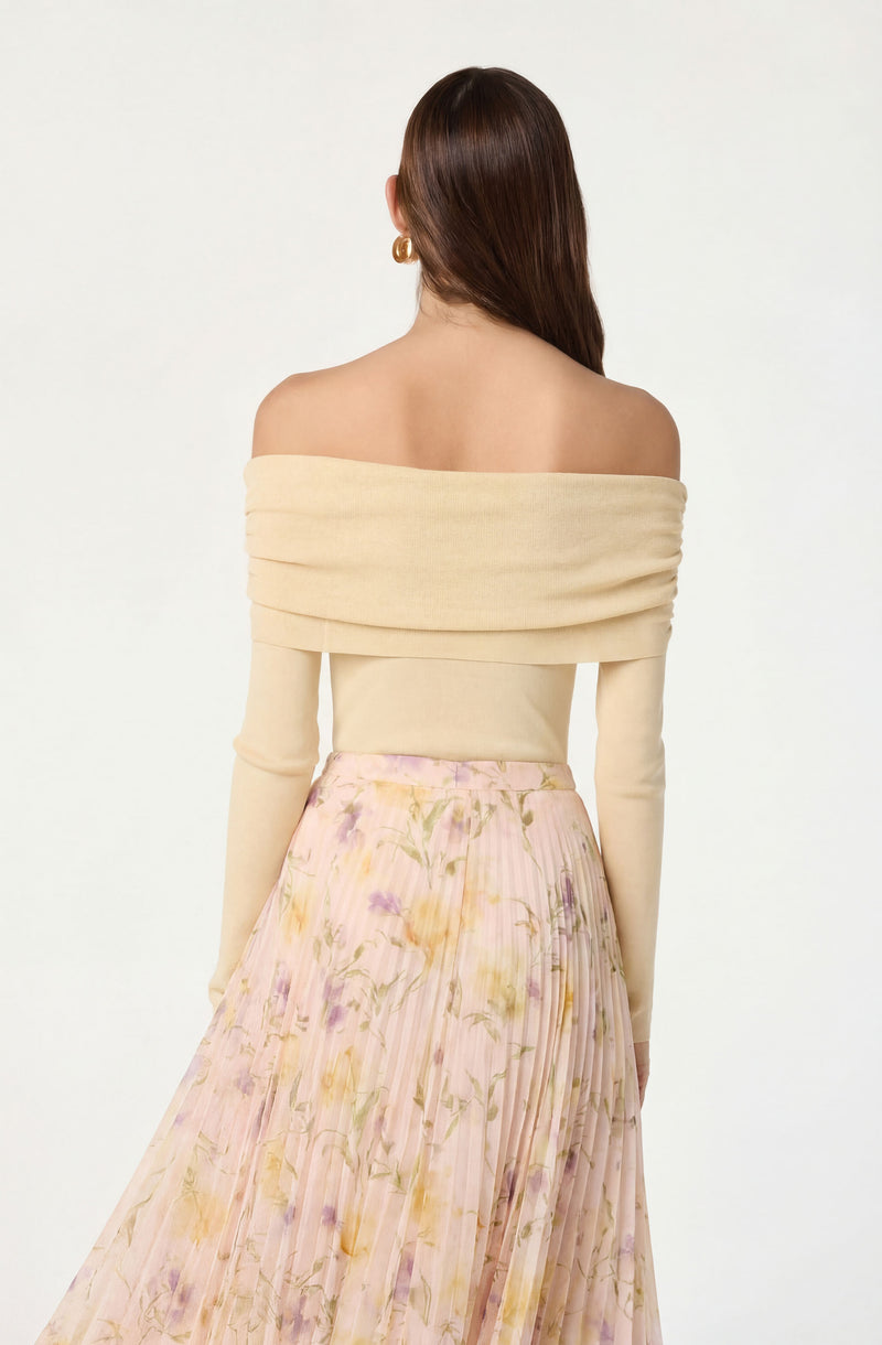 Woman wearing an off-the-shoulder beige sweater with long sleeves and a pink floral pleated skirt.