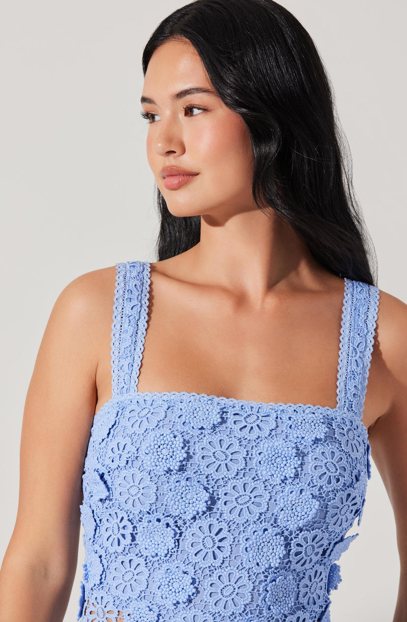 A woman is wearing a light blue sleeveless top made of lace with floral cut-out patterns. The top has wide straps also decorated with lace.
