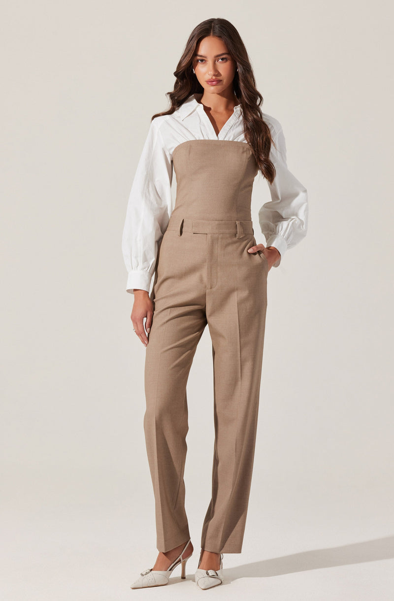 A woman is wearing high-waisted beige trousers with a fitted bodice overlay, paired with a white long-sleeve button-up shirt with puffed sleeves and a collar. She completes the outfit with white pointed-toe high heels.