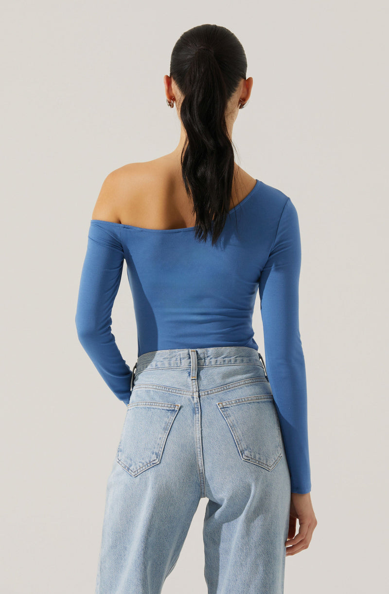 A woman is wearing a fitted, off-the-shoulder, long-sleeve top in a bright blue color. She pairs it with high-waisted, light-wash denim jeans.