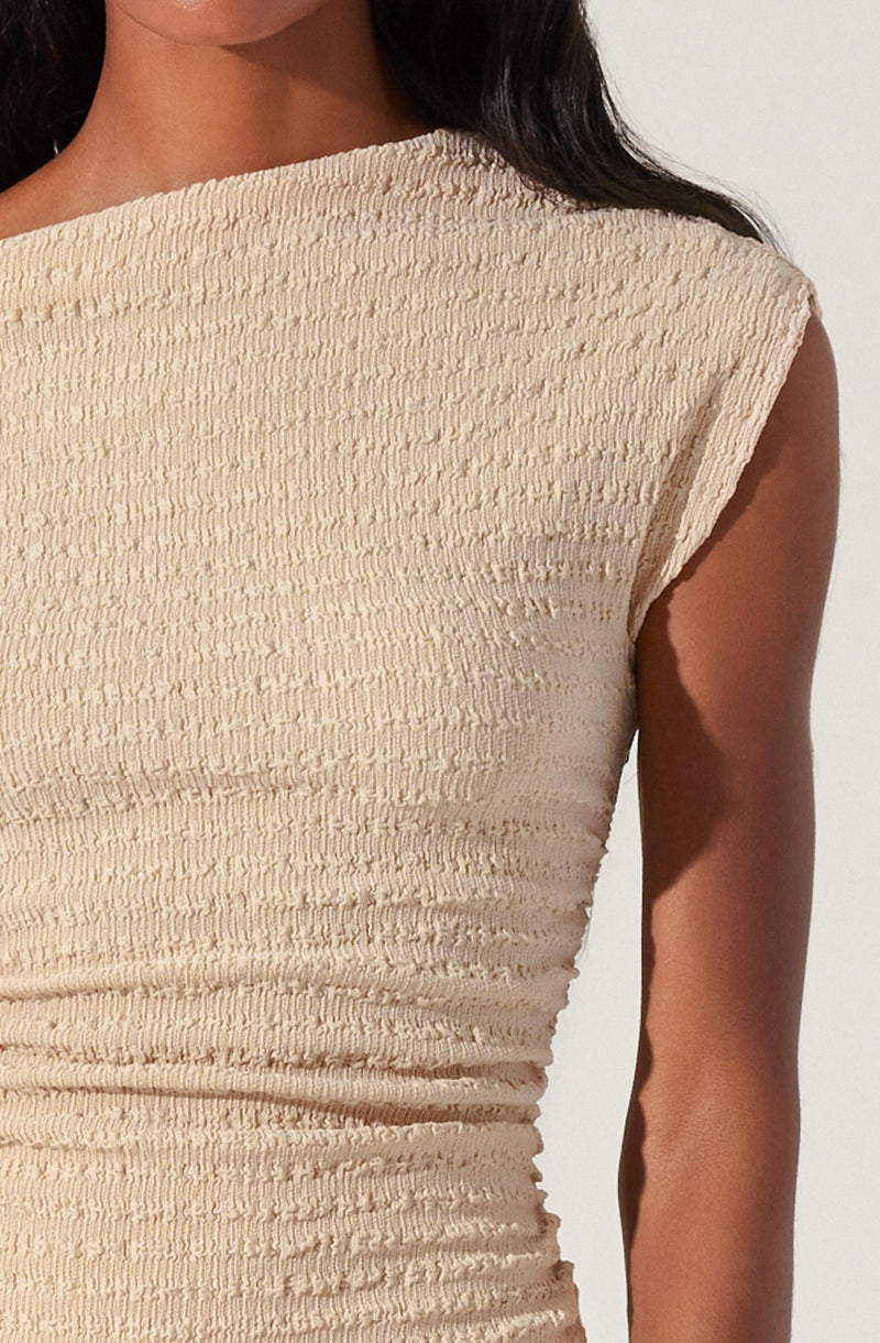 A person is wearing a sleeveless, beige textured top with a wide neckline. The fabric has a gathered, ribbed appearance, creating a streaked look. The shoulder edge is slightly rolled, and the top fits snugly around the torso.