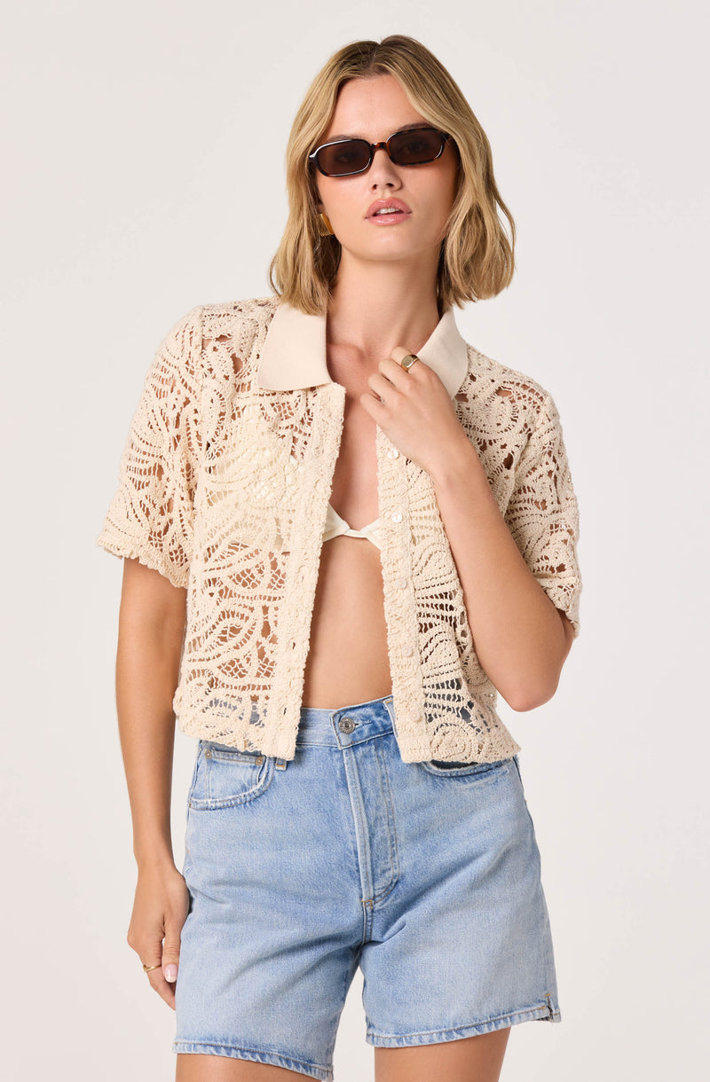 Woman wearing a beige crocheted short-sleeve jacket, cream top, and light blue denim shorts.