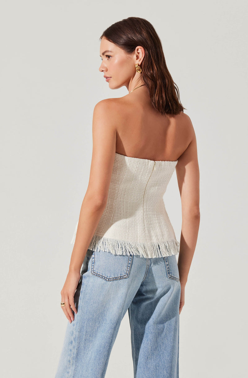 A woman wearing a strapless, textured, cream-colored top with a frayed hem. She is also wearing light blue, high-waisted jeans with a loose fit. She has gold hoop earrings and a simple ring on her left hand.