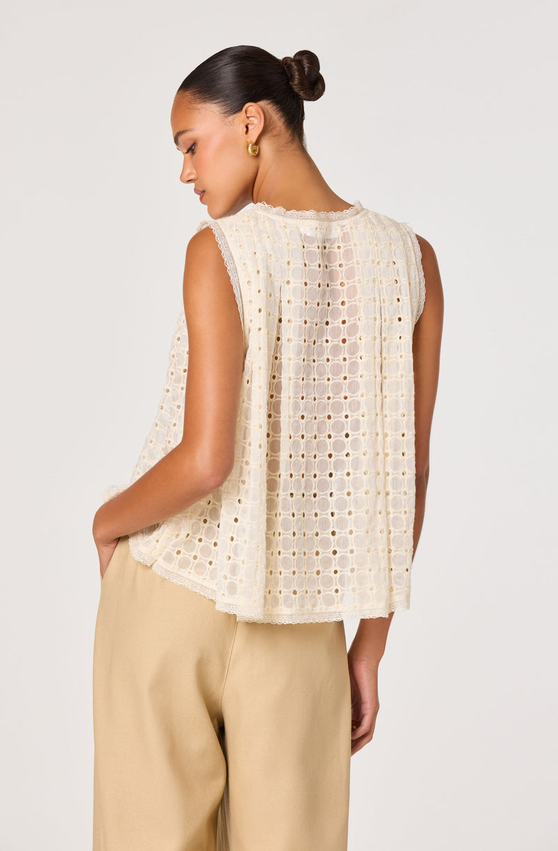 Woman in sleeveless cream eyelet lace top and beige pants, facing away.