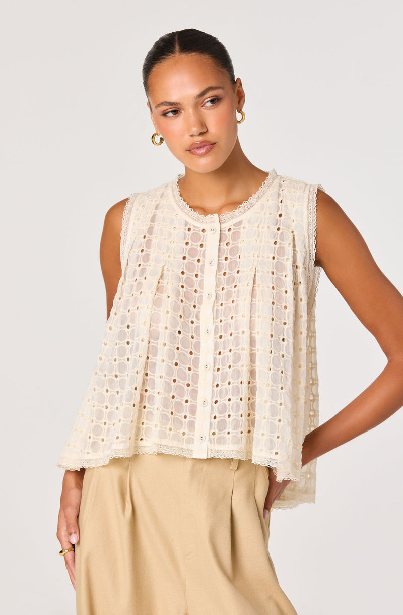 Woman wearing a sleeveless, cream-colored, eyelet crochet top with scalloped edges.