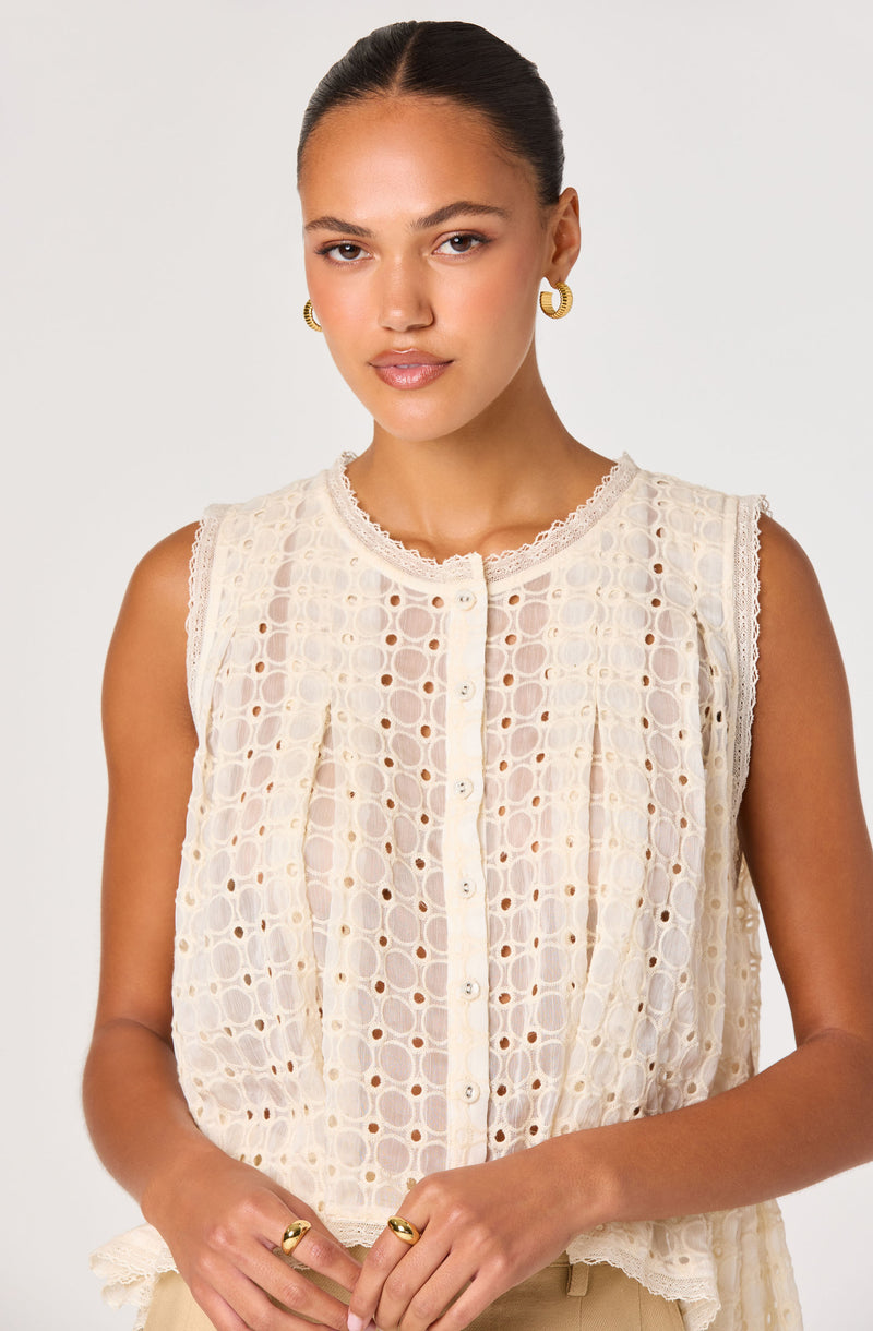 Woman wearing sleeveless cream blouse with eyelet pattern and lace trim, button-up front.