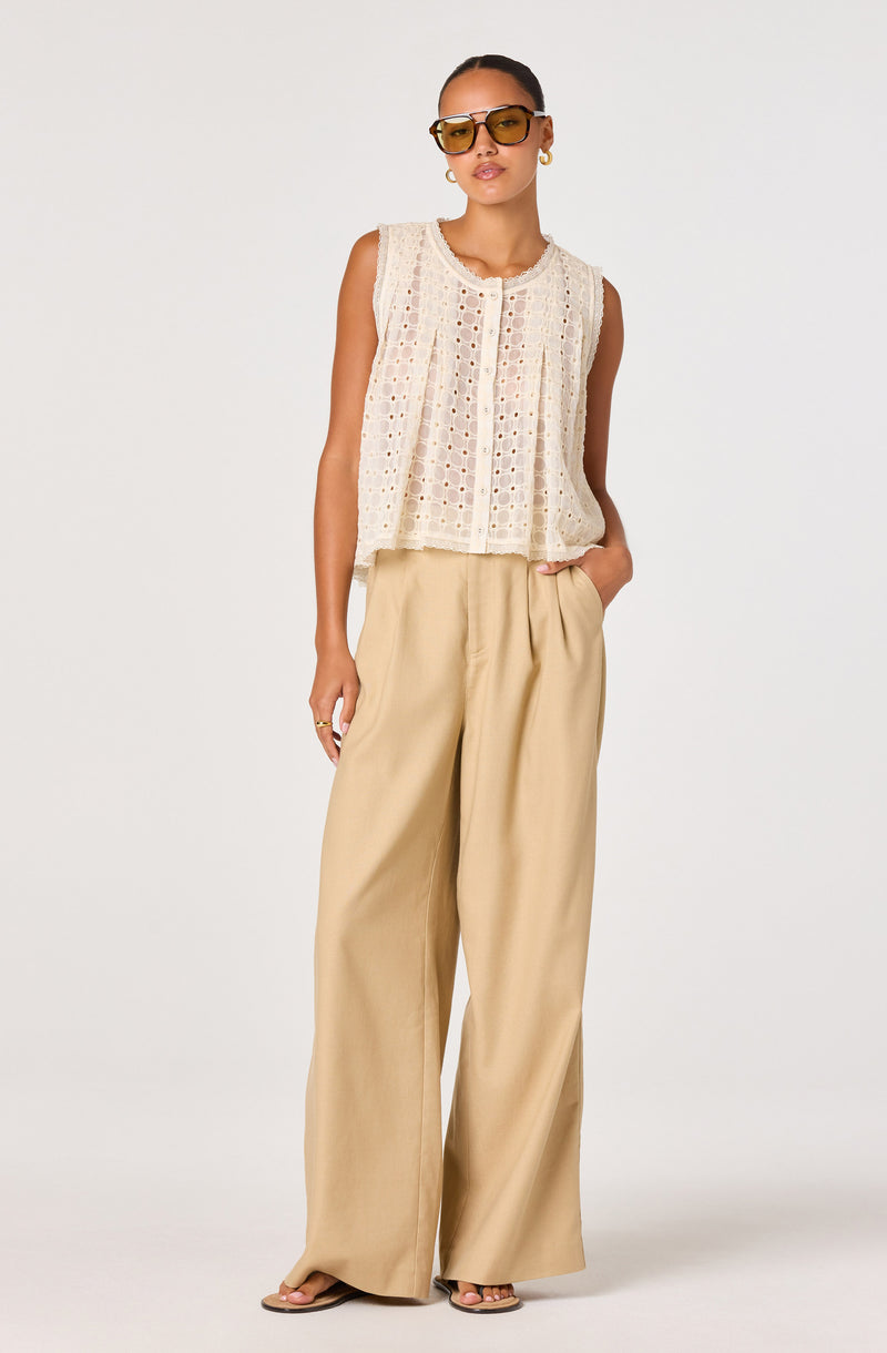 Woman wearing a sleeveless, cream-colored crochet top and wide-leg beige pants.