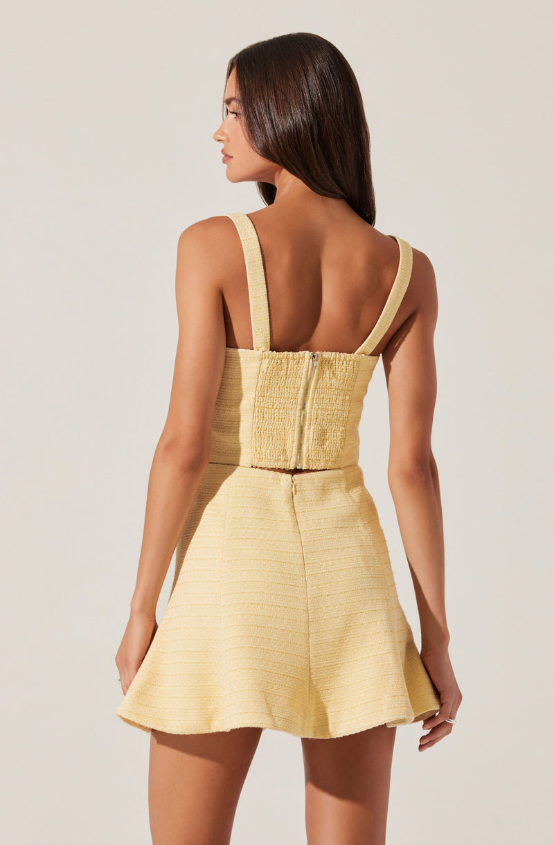 The outfit consists of a sleeveless, yellow textured top with thick straps and a zipper at the back, paired with a matching yellow textured skirt that flares out slightly from the waist. The fabric appears to have a woven pattern, giving it a structured look.