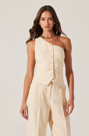 A woman is wearing a sleeveless, off-white, beige-colored vest with front buttons and matching high-waisted, wide-leg pants. The outfit appears to be made of a lightweight, textured fabric. She has accessorized with gold hoop earrings and a chunky gold chain necklace.