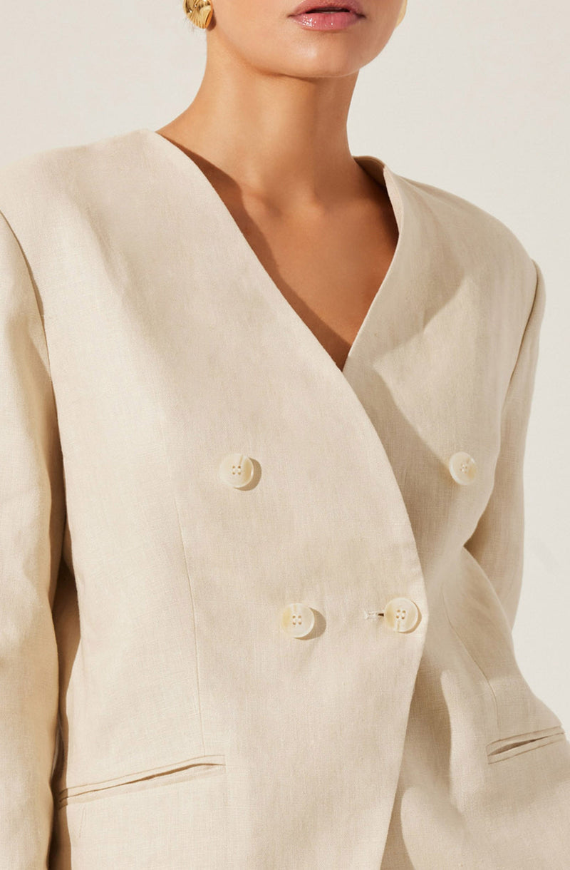 A woman is wearing a cream-colored double-breasted blazer with a notched lapel. The blazer features four buttons in two parallel rows on the front. The fabric appears to be lightweight with a smooth texture.