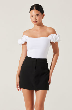 A woman is wearing an off-the-shoulder white top with ruffled short sleeves and a fitted bodice, paired with a high-waisted black skirt.
