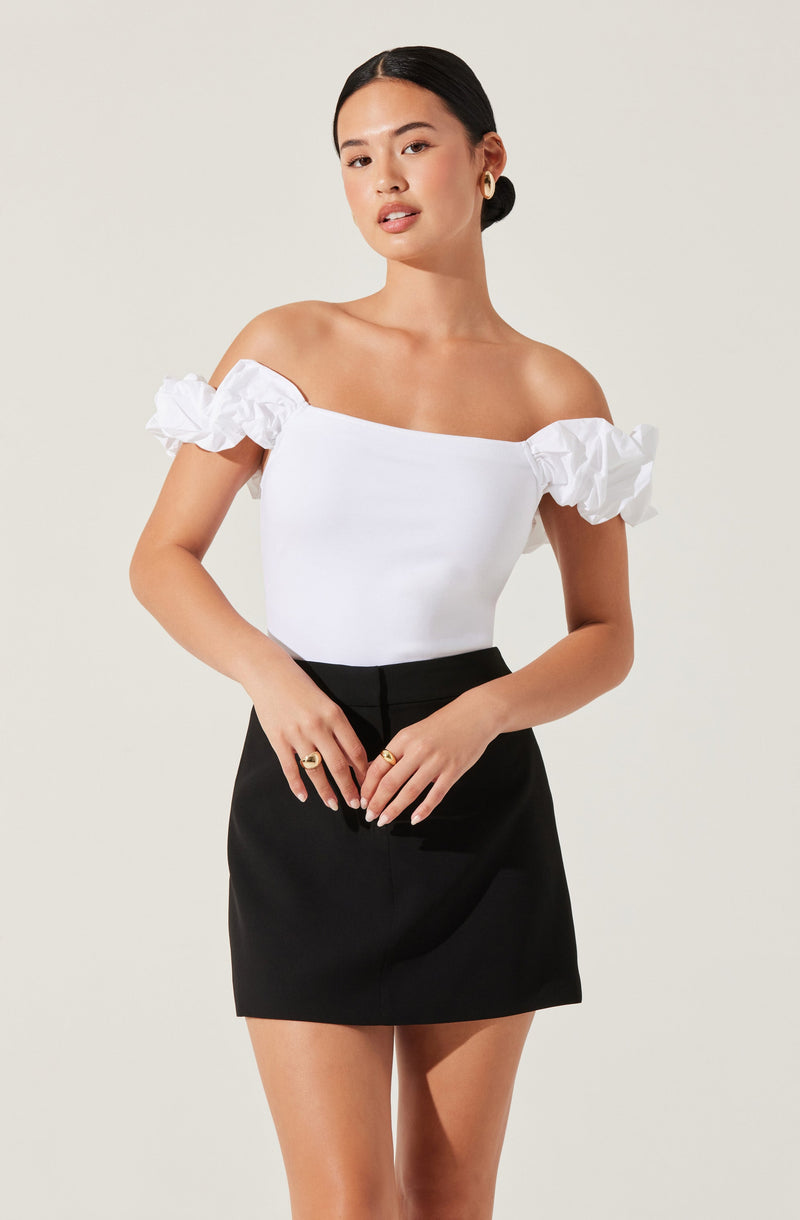A woman is wearing an off-the-shoulder white top with ruffled sleeves and a fitted black skirt.