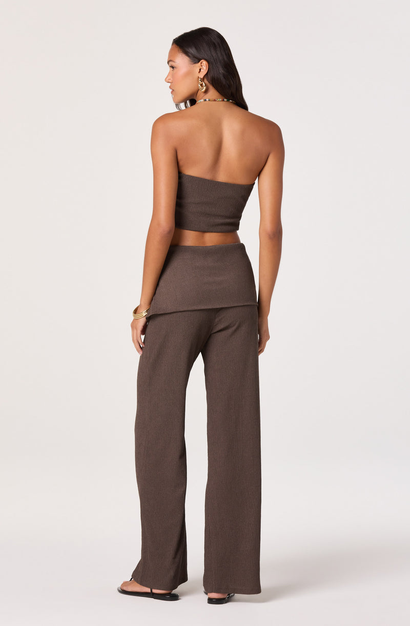 Woman in brown sleeveless top and wide-leg pants, facing away, with jewelry.
