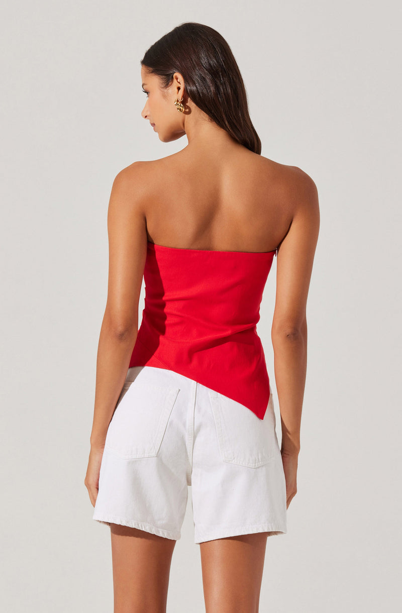 A woman wearing a strapless, fitted red top that is asymmetrical at the hem, paired with high-waisted white shorts that have large back pockets.