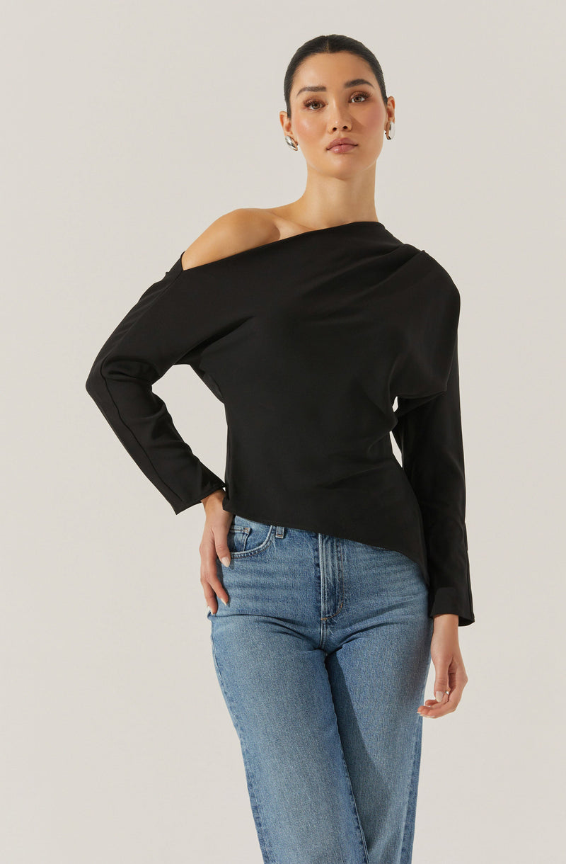 A woman is wearing a black, off-the-shoulder long-sleeve top and light blue jeans. The top has a loose fit and drapes gently over her shoulders, leaving one shoulder exposed. The jeans are high-waisted with a classic five-pocket design.