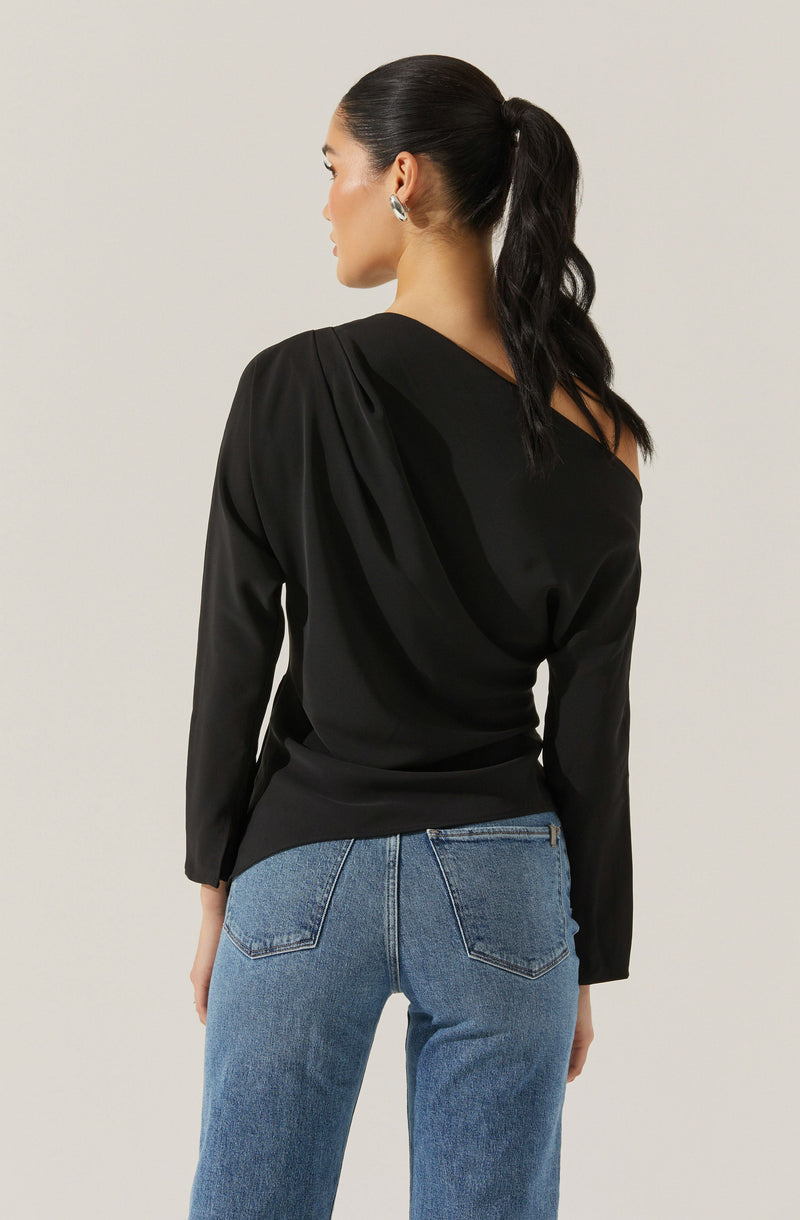 A woman is wearing a black long-sleeve top with a one-shoulder design and pleated detailing on the shoulder. She is also dressed in light blue high-waisted jeans with back pockets.