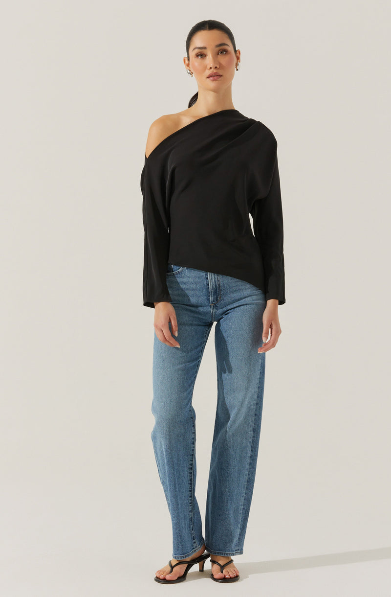 A woman is wearing a black off-the-shoulder top with long sleeves that drapes over one shoulder, paired with high-waisted, straight-leg blue jeans. She is also wearing black strappy heels.
