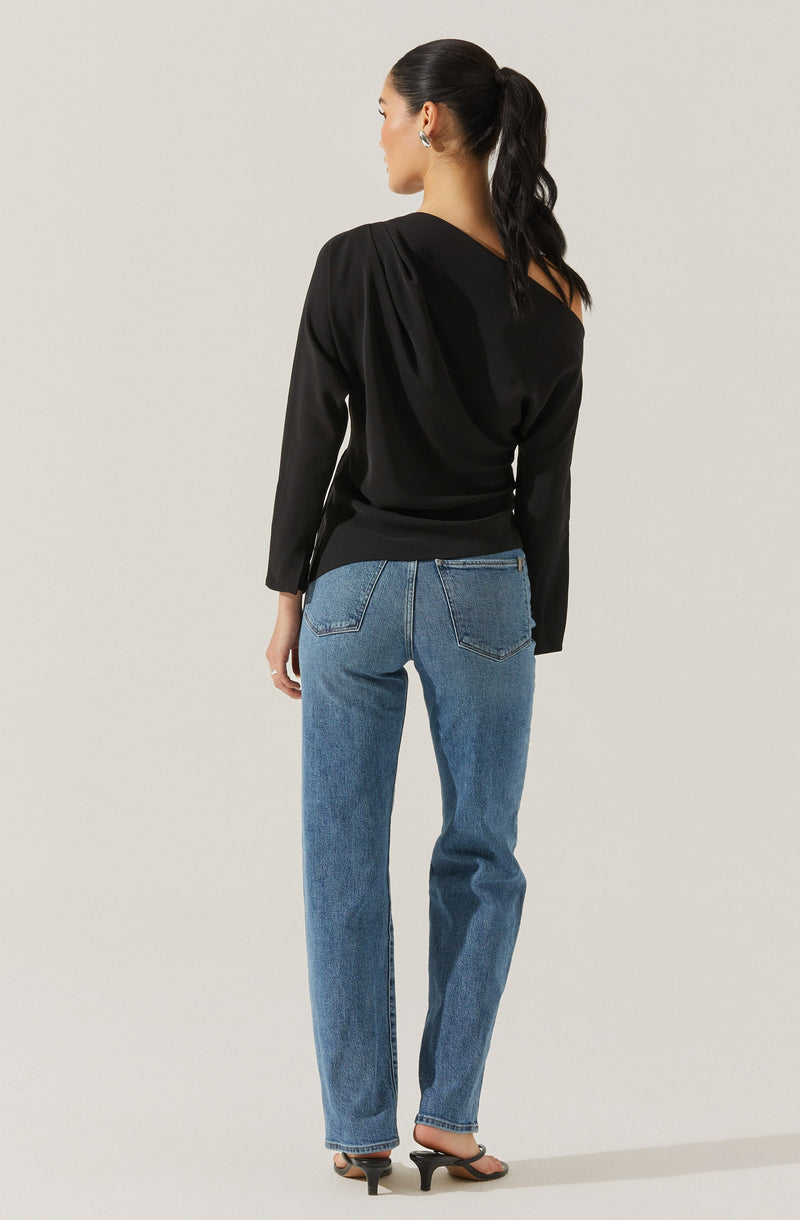 A woman is wearing a black long-sleeve top with a draped design on one shoulder and fitted at the waist. She is pairing it with high-waisted, straight-leg blue jeans and black open-toe high-heeled sandals. Her hair is styled in a sleek ponytail.