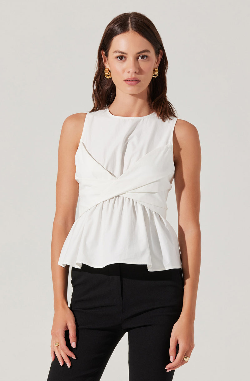 A woman is wearing a sleeveless white top with gathered and draped fabric details at the front, creating a layered, textured look. The top has a relaxed fit with a peplum-style hem that slightly flares out. She pairs the top with black pants.