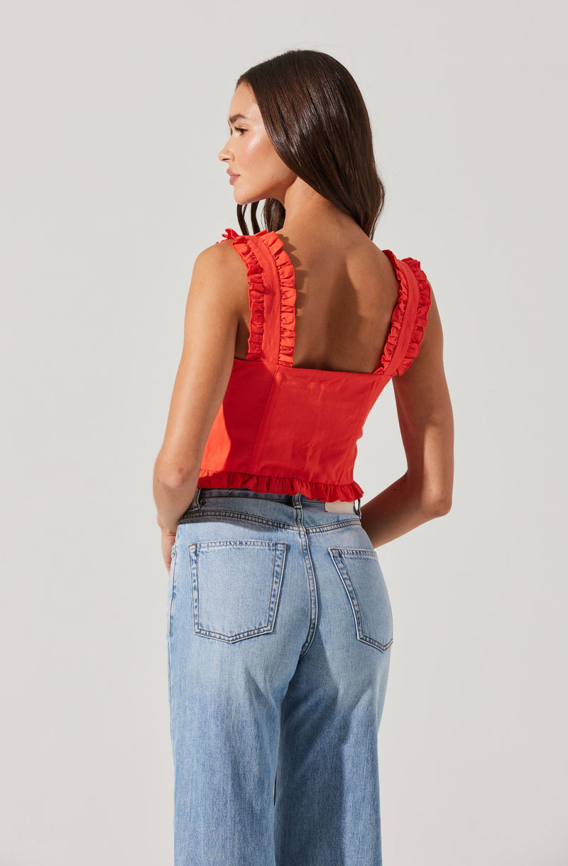 A woman is wearing a sleeveless red top with ruffled straps and ruffle detailing at the hem. She is also wearing high-waisted, light-wash jeans with prominent back pockets.