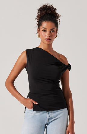 A woman is wearing a black sleeveless top with an asymmetrical, draped design that features a twisted knot detail on one shoulder. She pairs it with light-wash jeans.