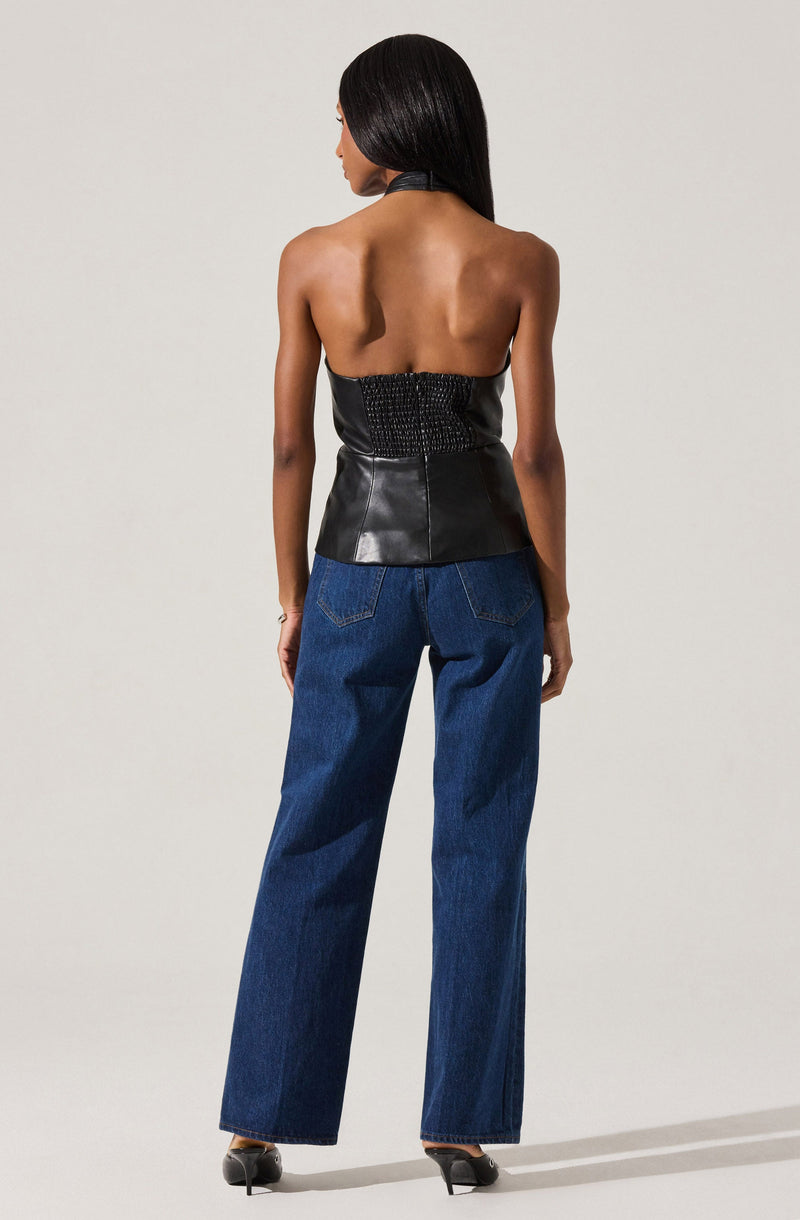 A woman is wearing a sleeveless, strapless black leather top with textured details on the back. She pairs it with high-waisted, wide-leg blue jeans and black high-heeled shoes.