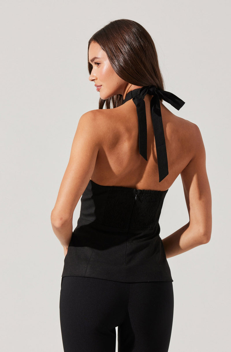 A woman is wearing a black halter top with a ribbon tie around the neck. The top is strapless in the back with a zipper closure. She is also wearing black pants.