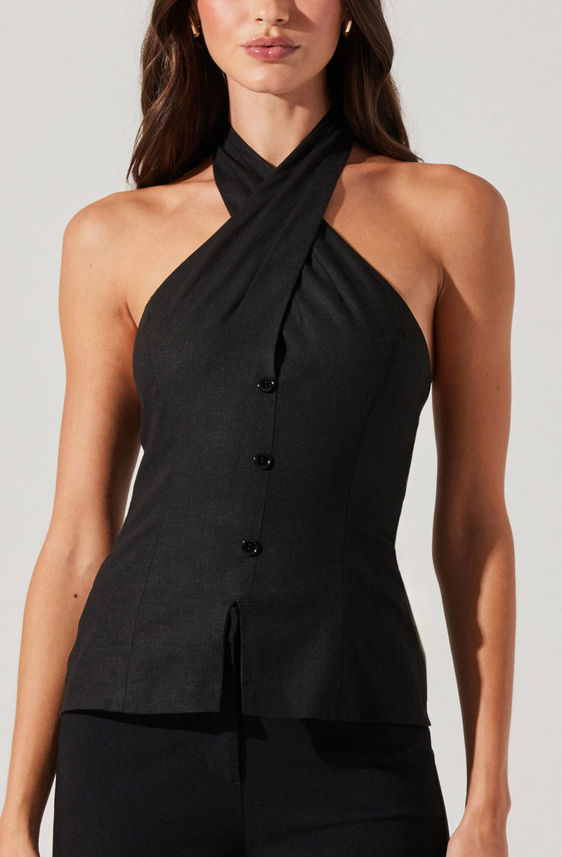 A woman is wearing a sleeveless black top with a high neckline that crosses over at the neck, creating a halter style. The top features a fitted silhouette with vertical seam lines and a front button closure with four black buttons. The fabric appears to have a slight sheen, giving it a sophisticated look.