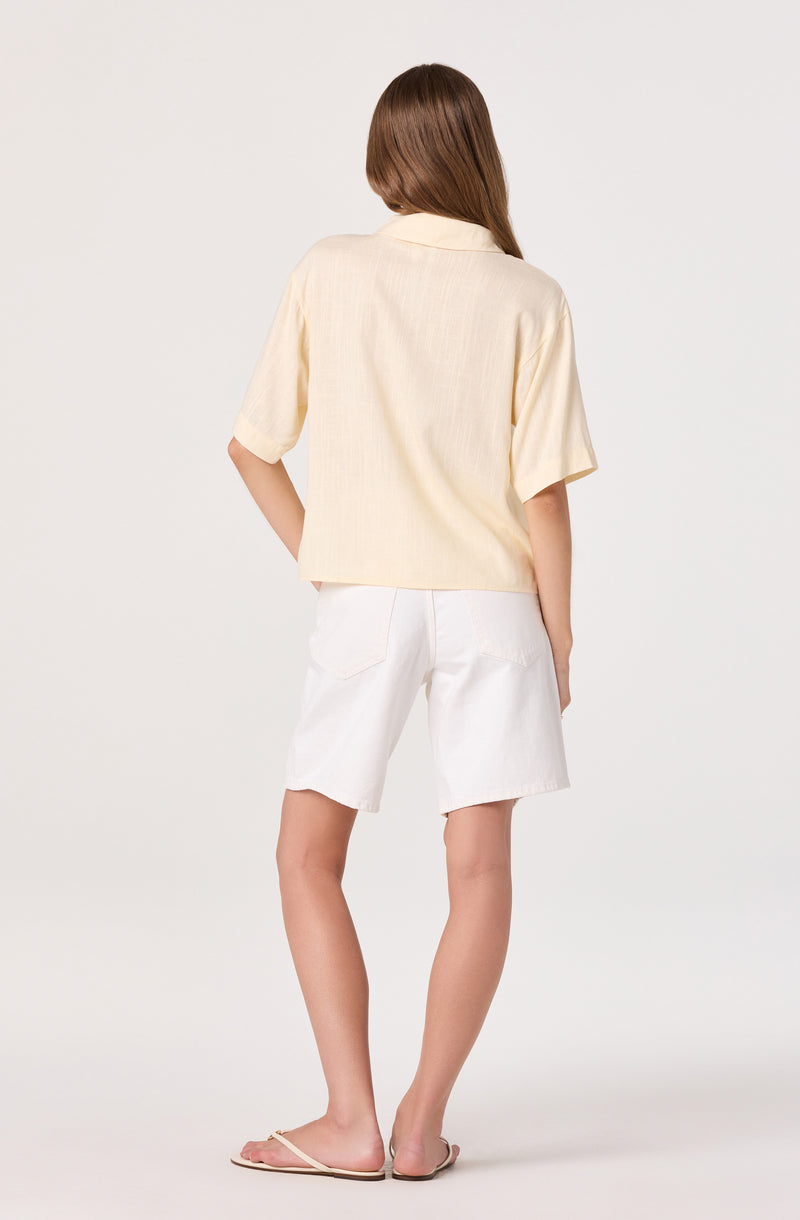 Woman wears a short-sleeve cream button-up shirt and white knee-length shorts.