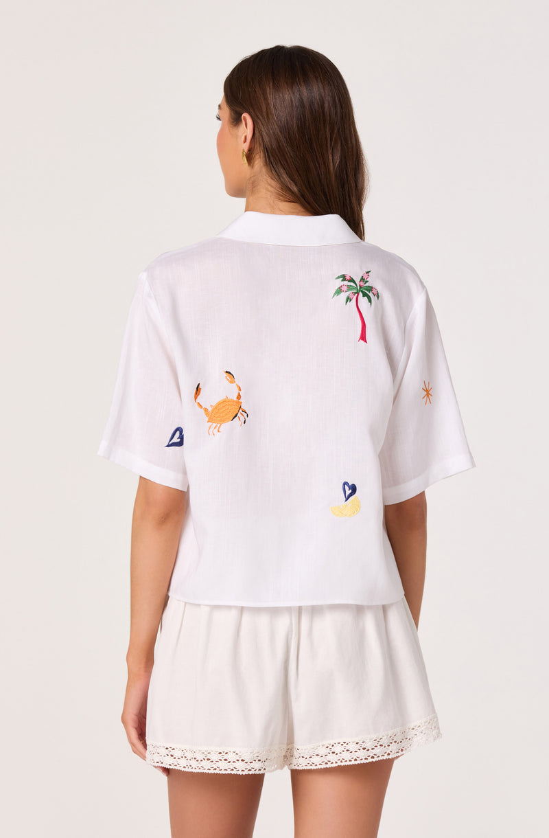 White short-sleeve shirt with colorful embroidered palm tree, crab, star, and heart designs.