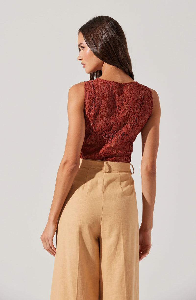 A woman is wearing a sleeveless, red lace top with a floral pattern, paired with high-waisted, wide-leg beige trousers.