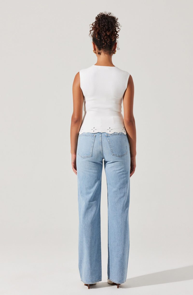 A woman is wearing a sleeveless white top with frayed edges at the hem, paired with light blue high-waisted, wide-leg jeans.