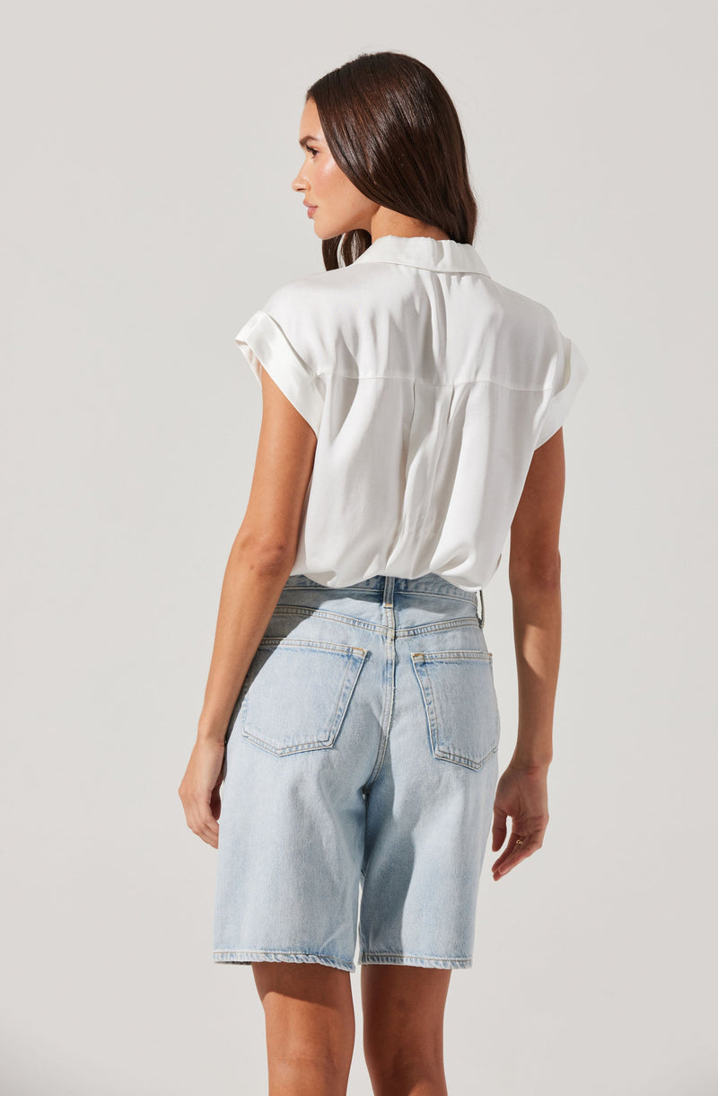A woman is wearing a white short-sleeve blouse with a loose fit and a collar, paired with light blue denim shorts that have a high waist and visible back pockets.