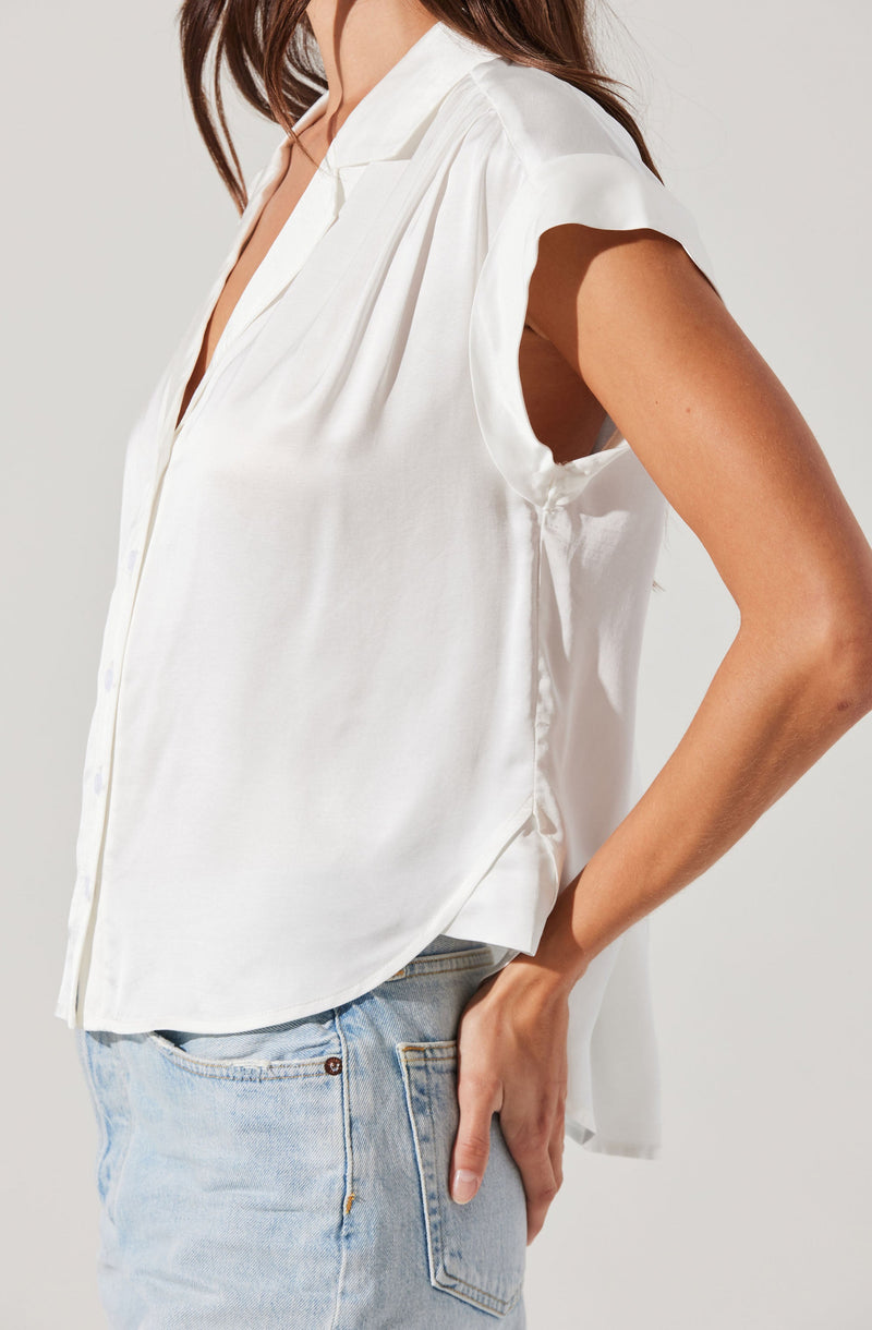 A woman is wearing a sleeveless, white satin blouse with a collar. The blouse has a loose fit and a smooth, shiny texture. She has paired it with light blue denim jeans.