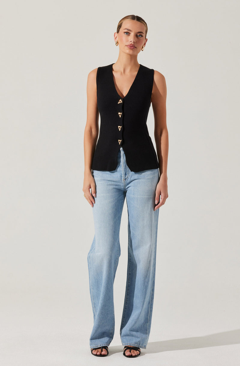 A woman is wearing a sleeveless black vest with a V-neckline, featuring gold triangle buttons down the front. She pairs the vest with light-wash, high-waisted, wide-leg jeans and black strappy sandals.