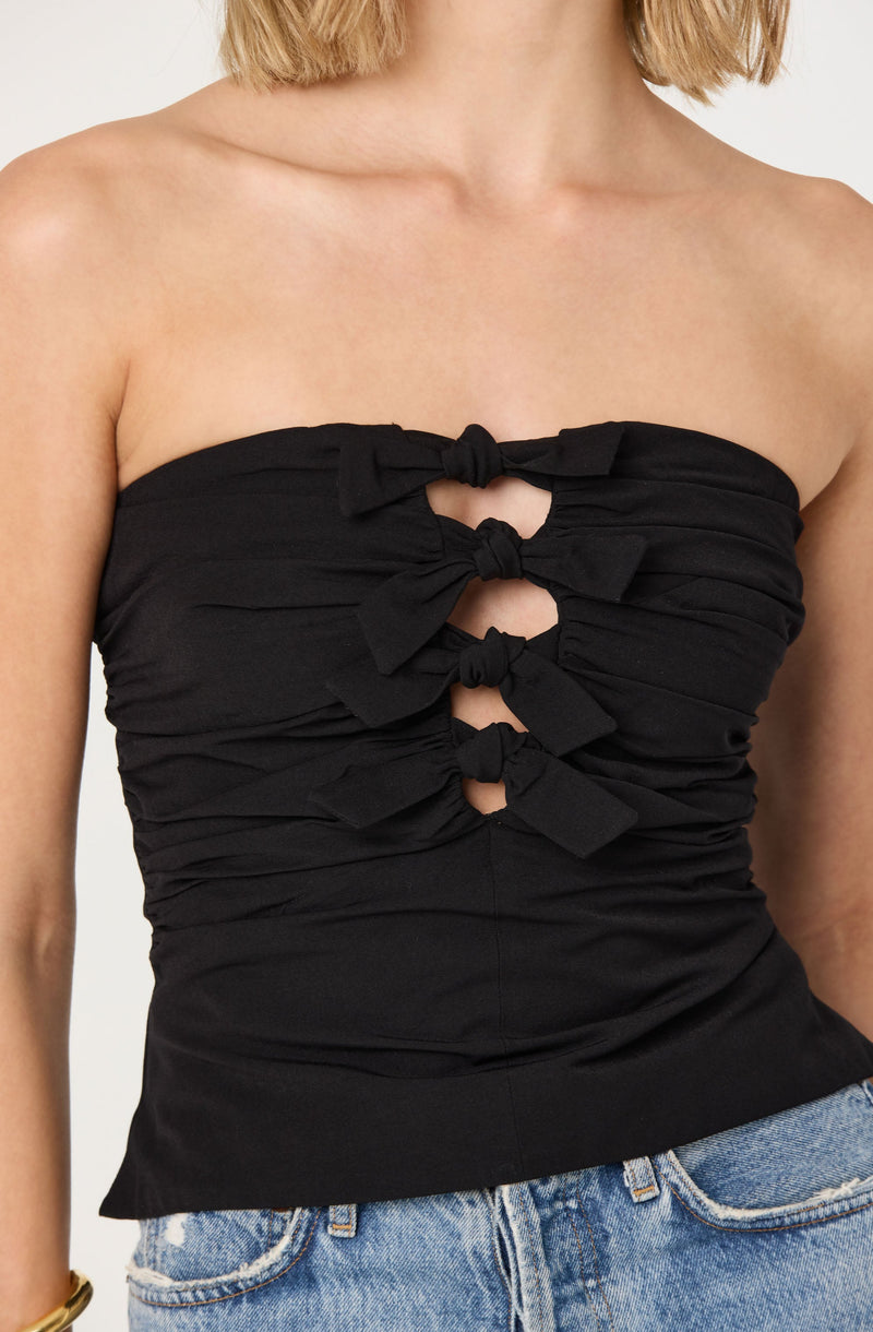 A woman is wearing a black, strapless top that features four bows arranged vertically down the front, creating a ruched and knotted appearance. The top is fitted and made of a soft, slightly stretchy fabric.