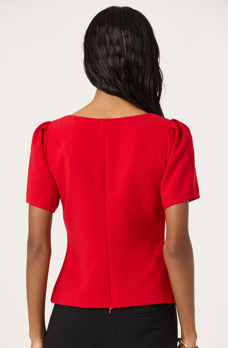 The blouse is red with a round neckline and short puffed sleeves. The fabric appears smooth and slightly shiny. The back of the blouse features a visible vertical seam down the center and a hidden zipper at the bottom.