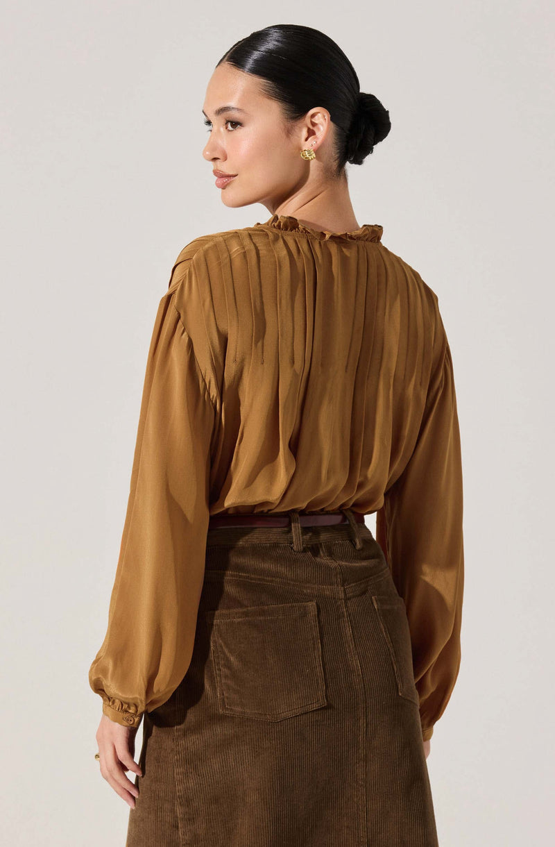 A woman is wearing a long-sleeved, silky, brown blouse with a gathered neckline and pleated details on the back. The blouse has slightly puffed sleeves with elastic cuffs. She is also wearing high-waisted, brown corduroy pants with front and back pockets.