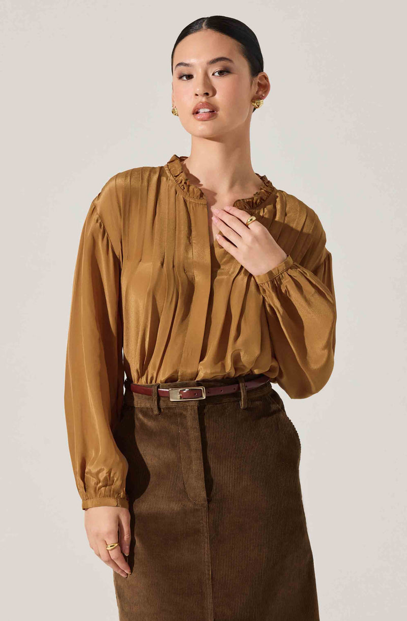 A woman is wearing a shiny, gold-brown satin blouse with a high ruffled collar and long puffed sleeves gathered at the wrists. She pairs it with a high-waisted, brown corduroy skirt that has a belt. She accessorizes with gold earrings and rings.