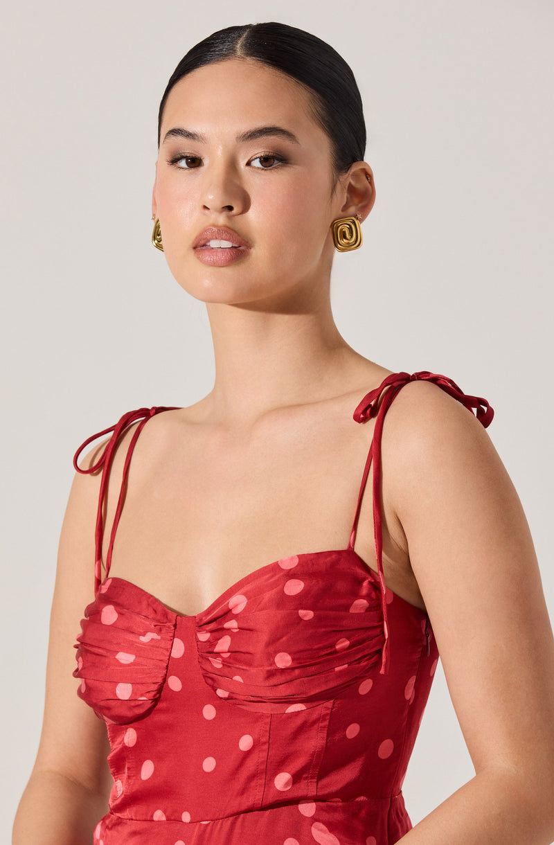 A woman is wearing a red sleeveless dress with thin shoulder ties. The dress features a ruched bust area with gathered fabric, decorated with pink polka dots throughout.