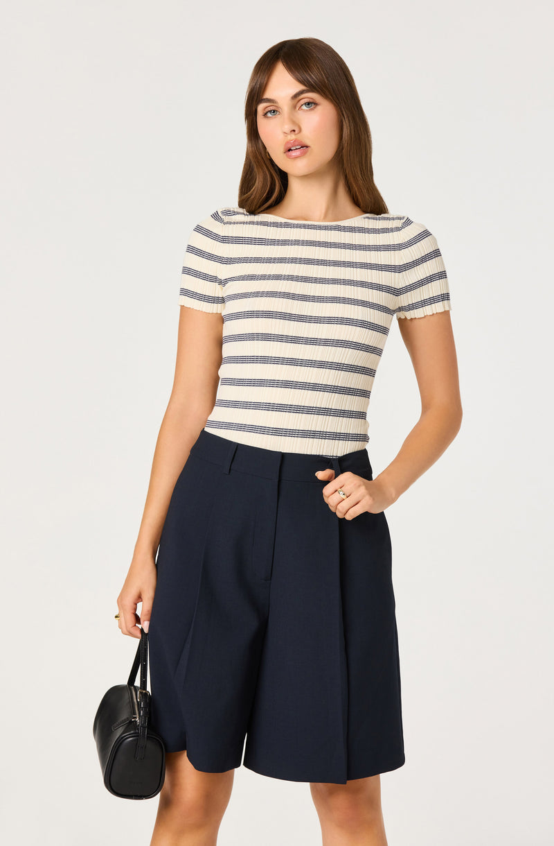 Woman wearing a cream and navy striped short-sleeve top and navy wide-leg shorts, holding a black handbag.