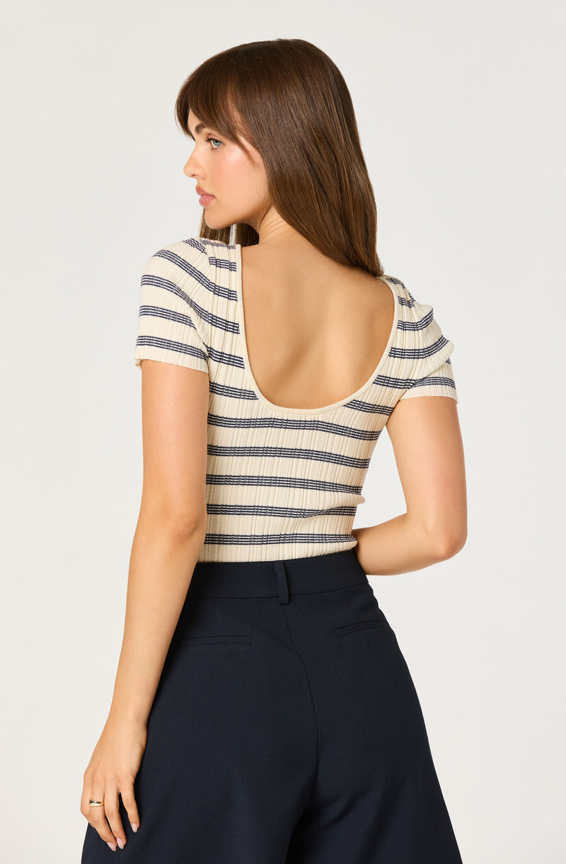 Woman in a cream and navy striped top with a wide scoop back and navy high-waisted pants.