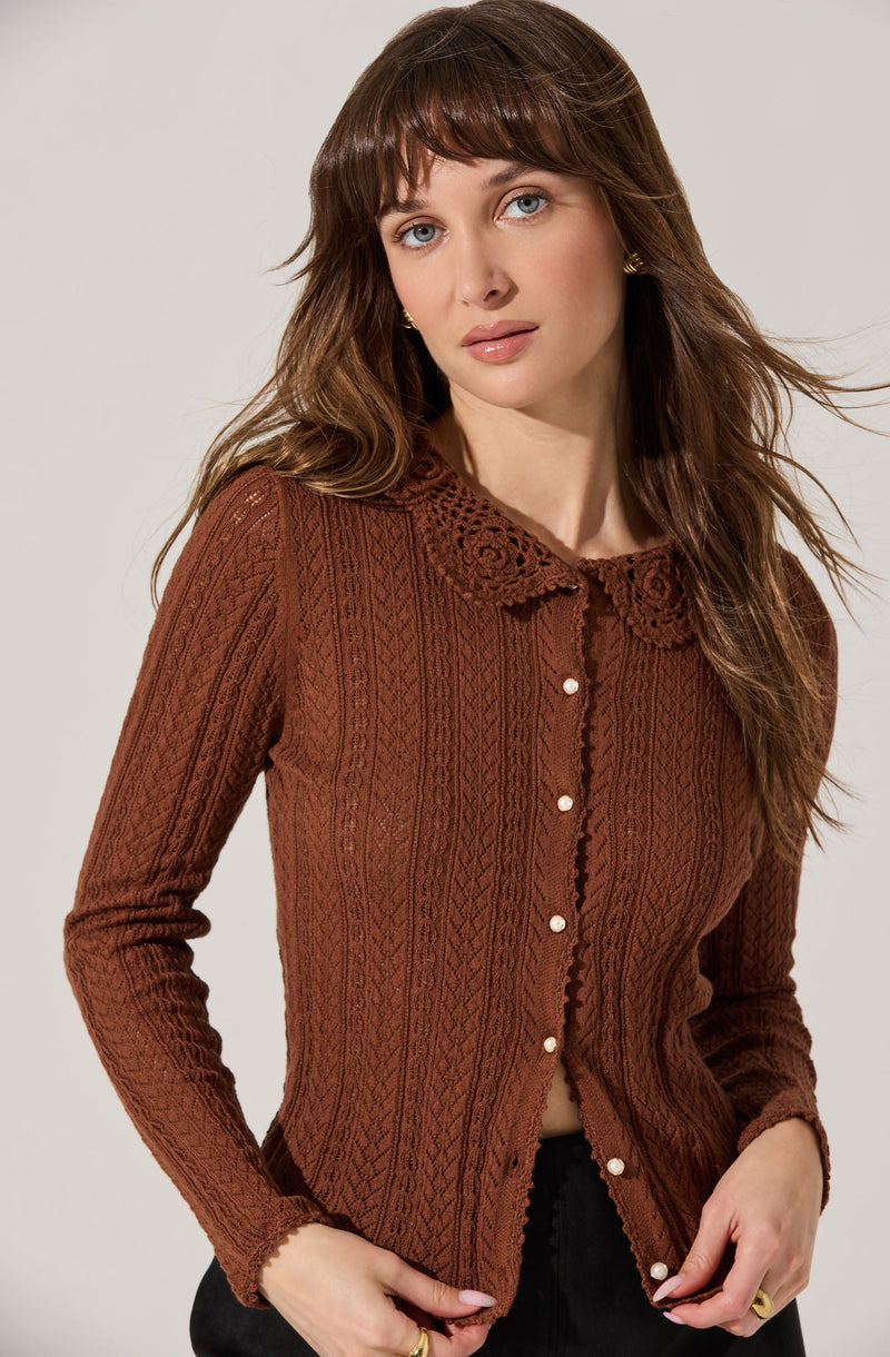 A woman wearing a brown, long-sleeved, cable-knit cardigan with a lace-trimmed collar and pearl buttons down the front.