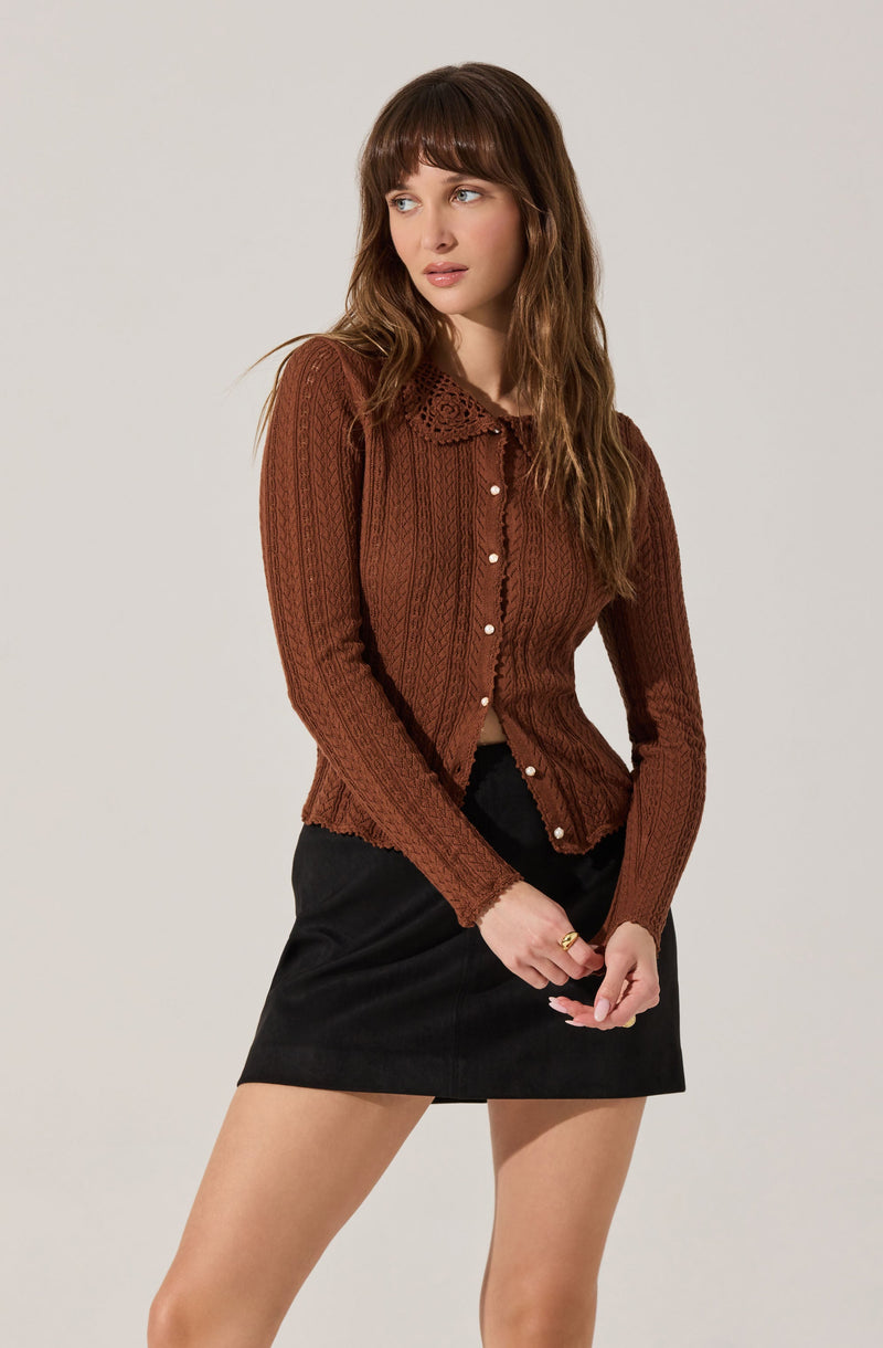 A woman is wearing a fitted, long-sleeved, ribbed brown cardigan with a lace collar and pearl buttons down the front.