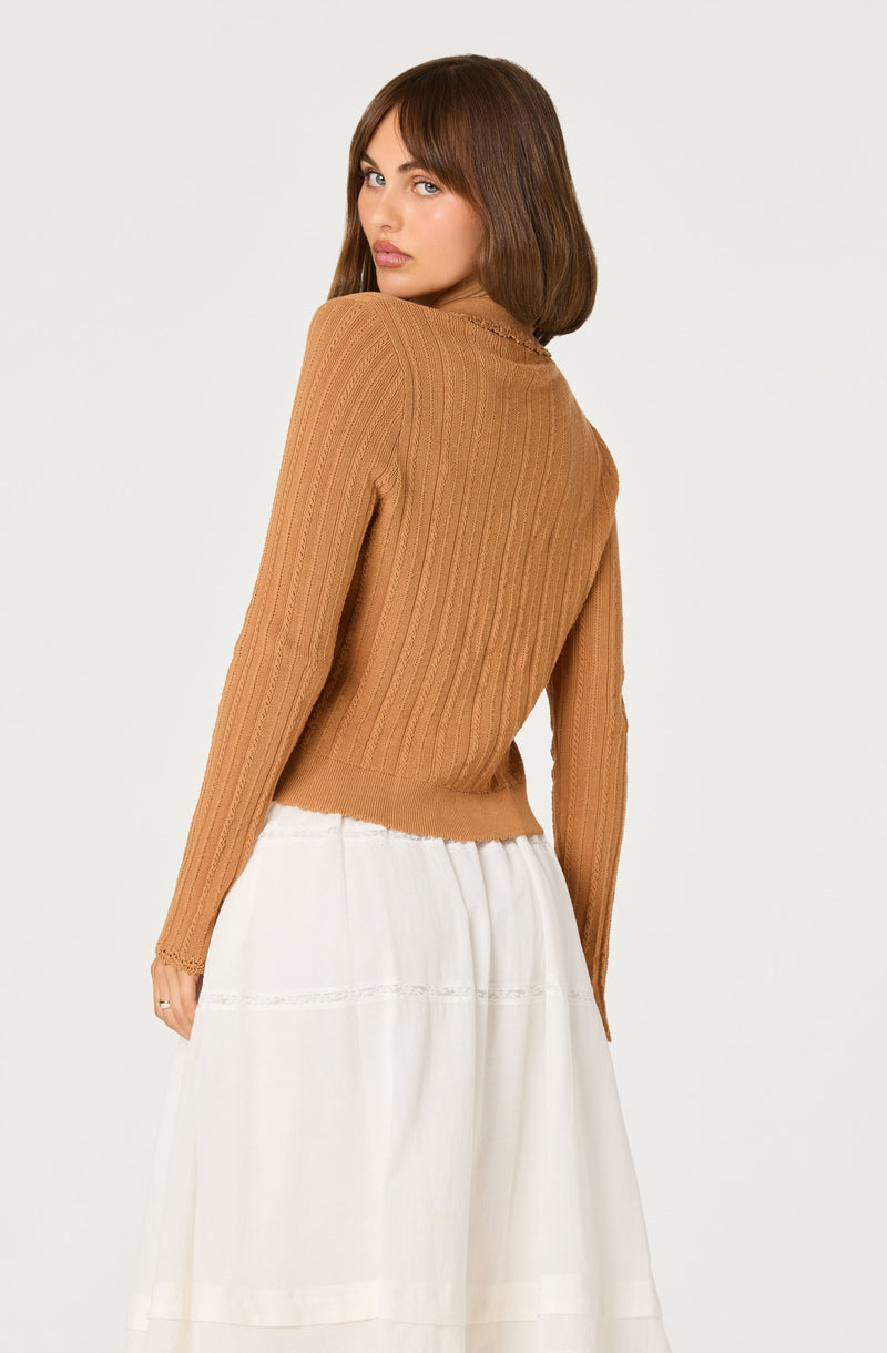 Woman wearing a tan ribbed long-sleeve sweater and a white skirt.