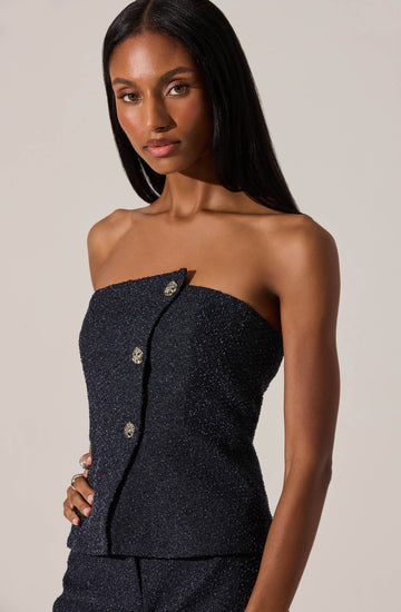 A woman is wearing a strapless black top and matching black pants, both made from a fabric with a sparkly, glittering texture. The top features a row of decorative gold buttons down the front.