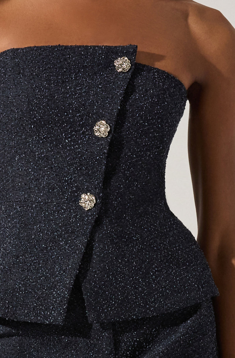 A close-up of a strapless black dress made of sparkly fabric with a subtle shimmer. The dress features a structured bodice with three decorative gold and silver buttons arranged vertically along the front. The fabric appears textured and glittery, adding an elegant touch.