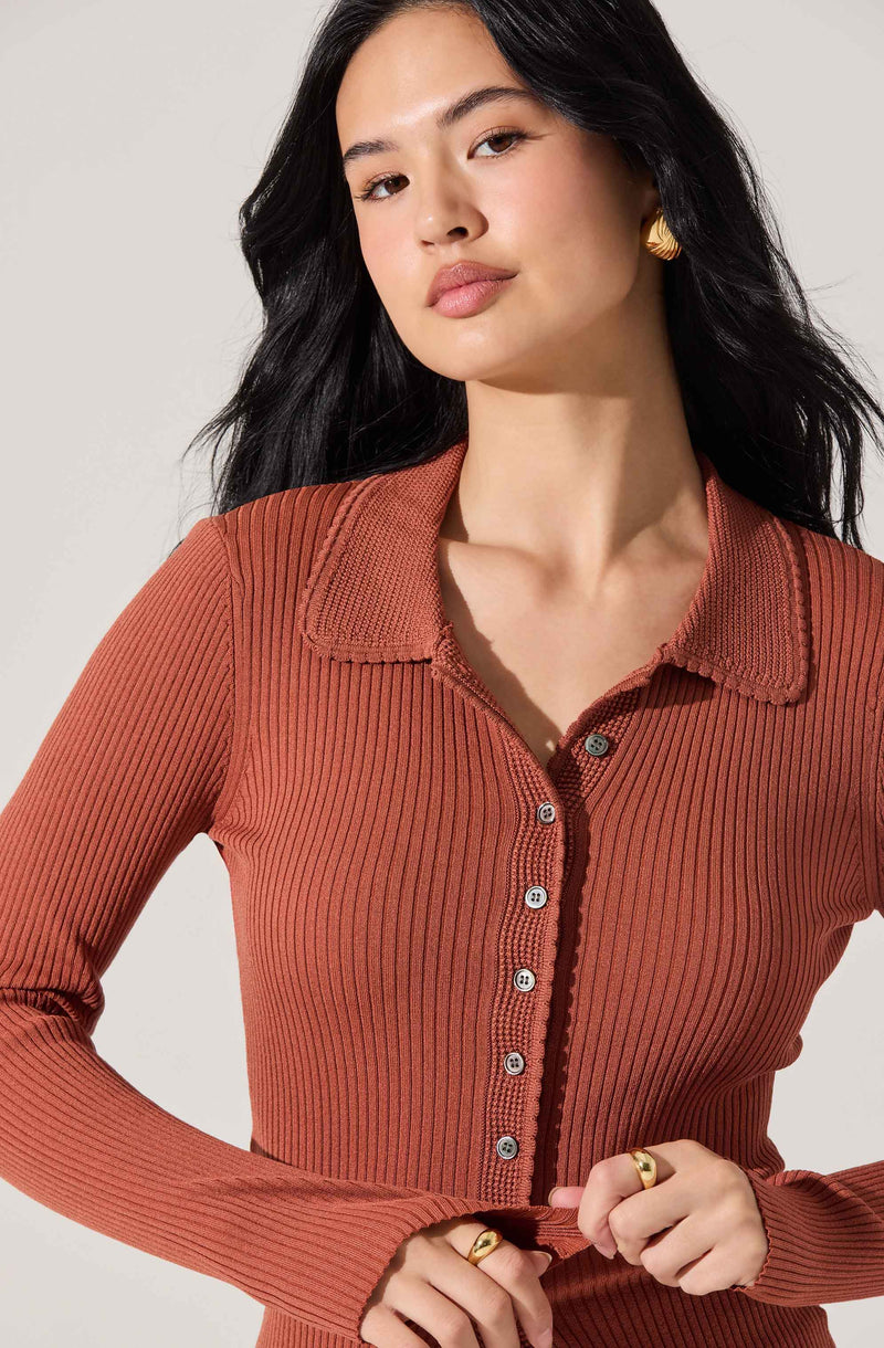 A woman is wearing a long-sleeved, ribbed, burnt orange shirt with a collared neckline. The shirt features a row of buttons down the front.