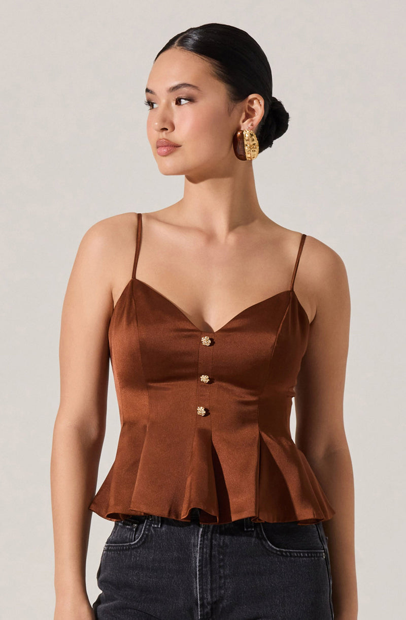 A woman is wearing a sleeveless, satin-like brown top with thin spaghetti straps. The top features a sweetheart neckline, decorative buttons down the front, and a pleated, ruffled hem.