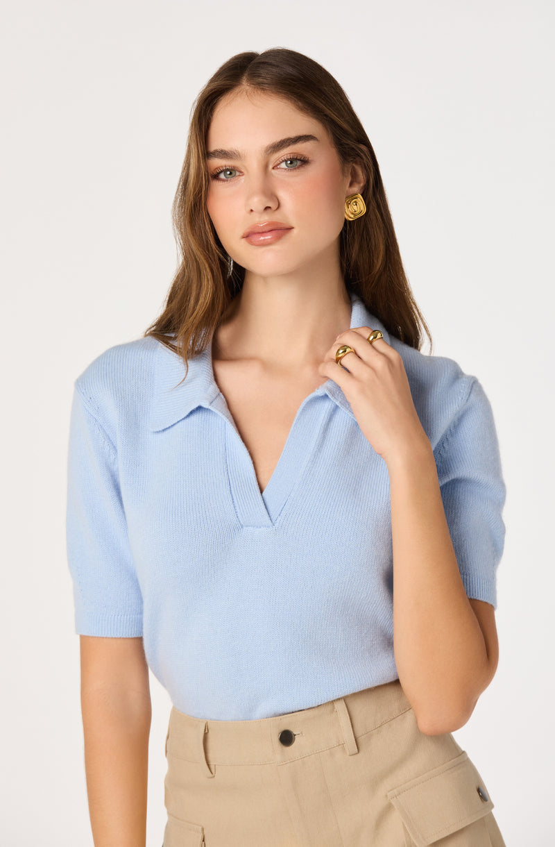 Woman wearing a light blue short-sleeve polo shirt and beige high-waisted pants.